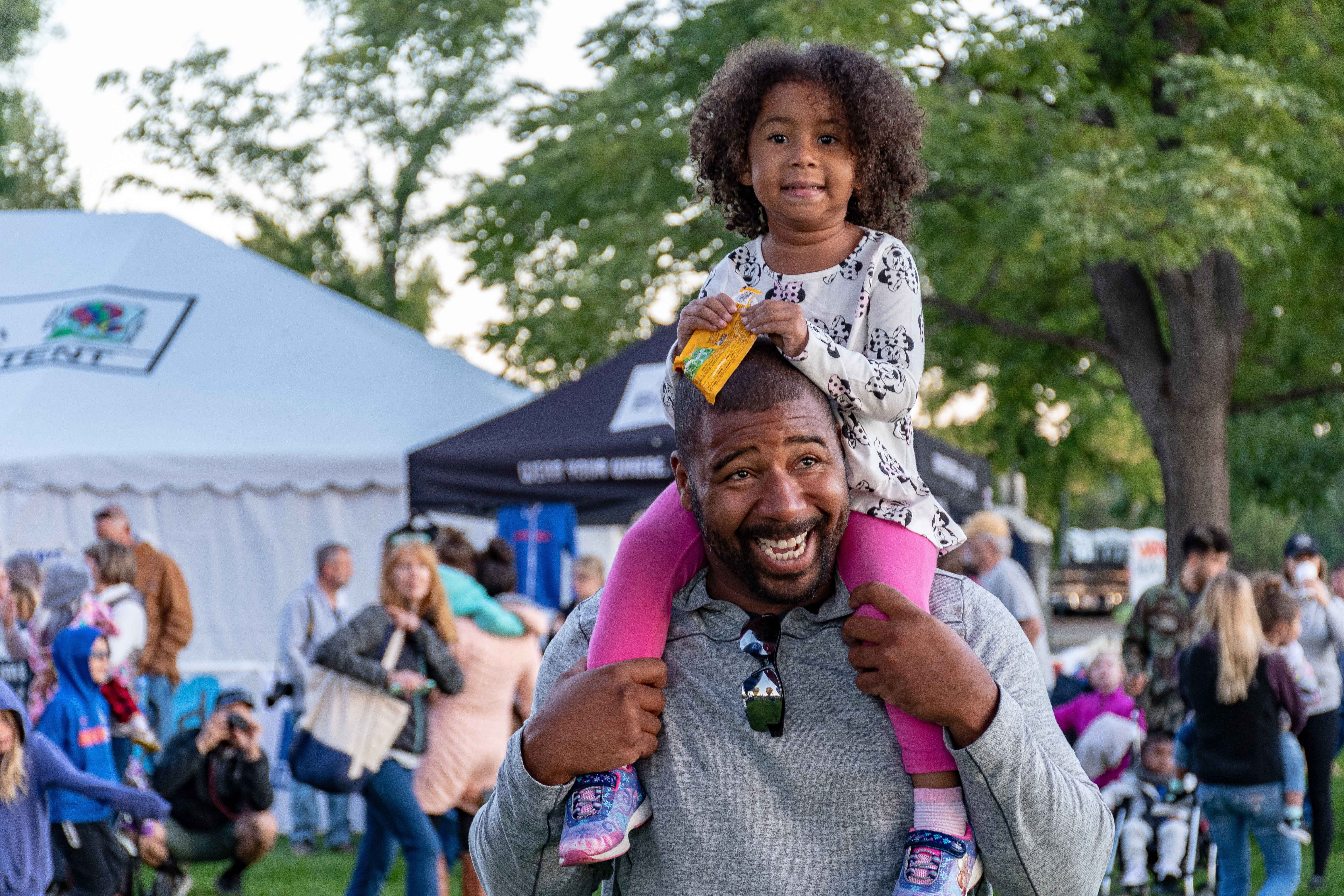 child sitting on parent's shoulders at an event